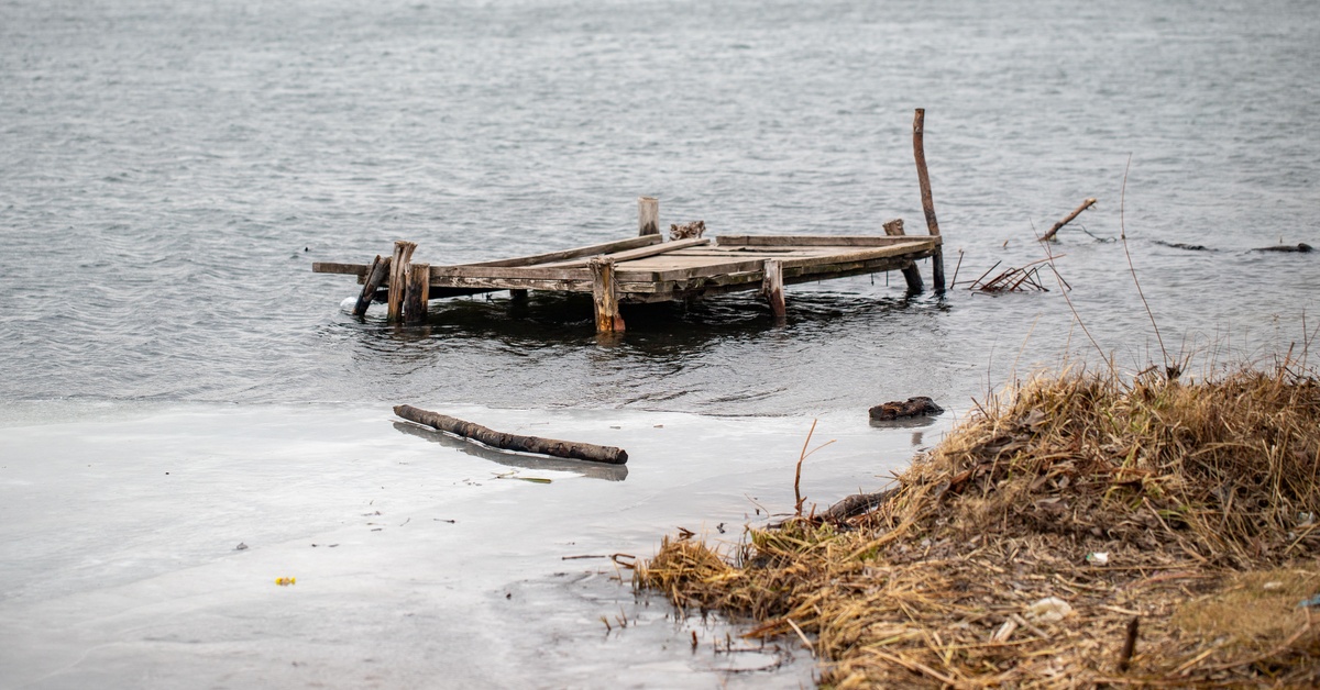 A shattered, old wooden dock floating out in the middle of the water amidst logs and other debris.