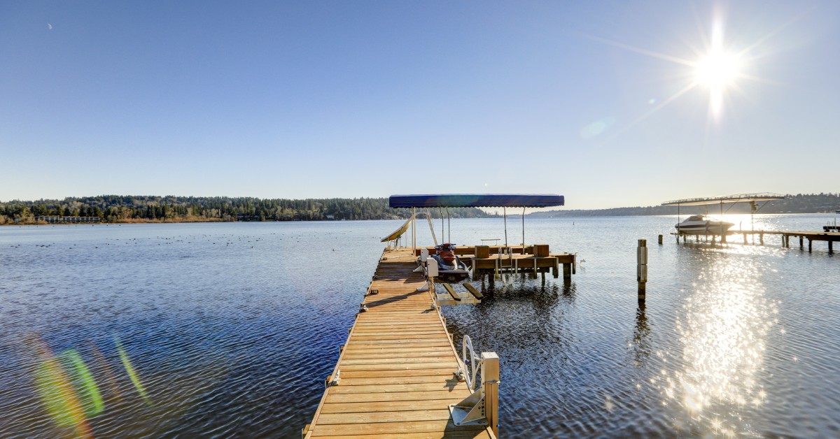 A view of a shimmering blue lake with a wooden deck extending out into the distance, with a small, covered boat lift at the end.