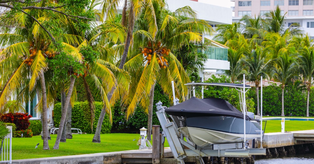 A small dock holding up a class 2 size boat. The dock is on the edge of a canal with palm trees lining the edge.