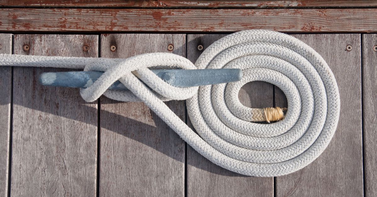 A top-down view of a thick, white line coiled and tied neatly to a boat cleat on a wooden dock.