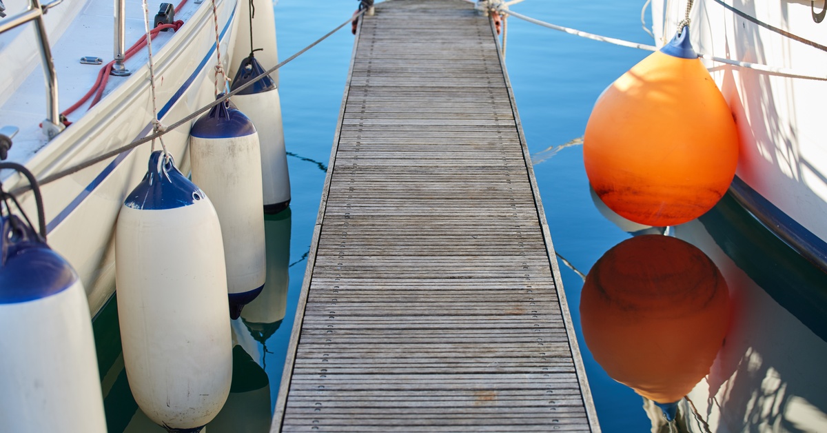 A focus shot of a small, floating wooden dock flanked by two anchored boats with buoys hanging from the sides.