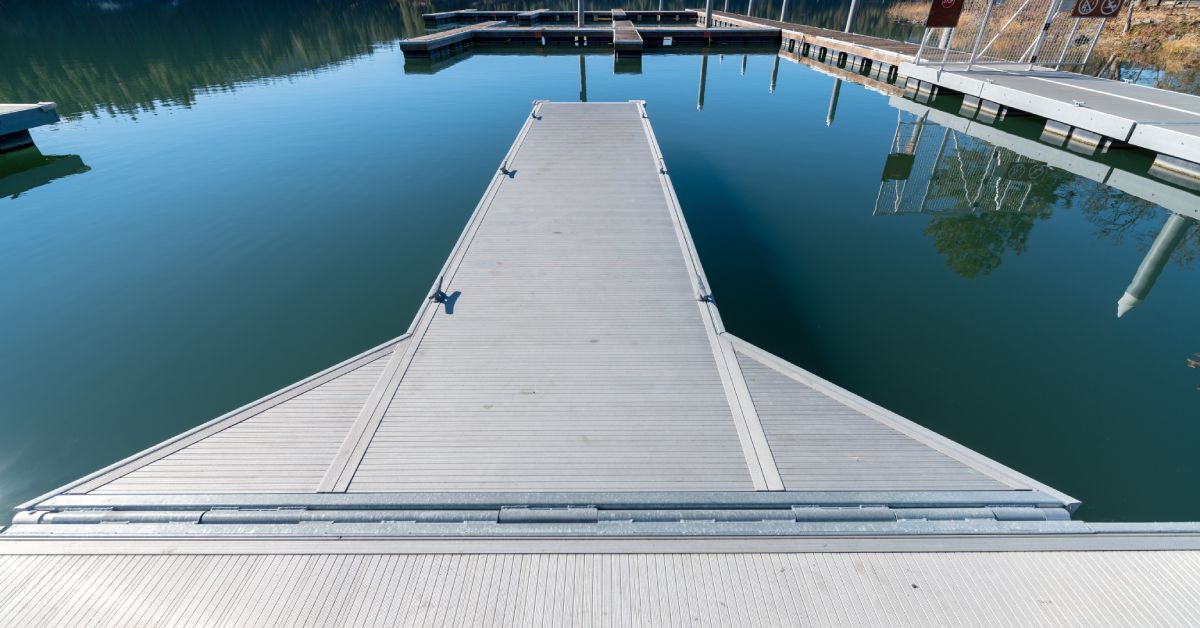 A long metal dock jetting out into the water. There are other docks around it and mountains in the distance.