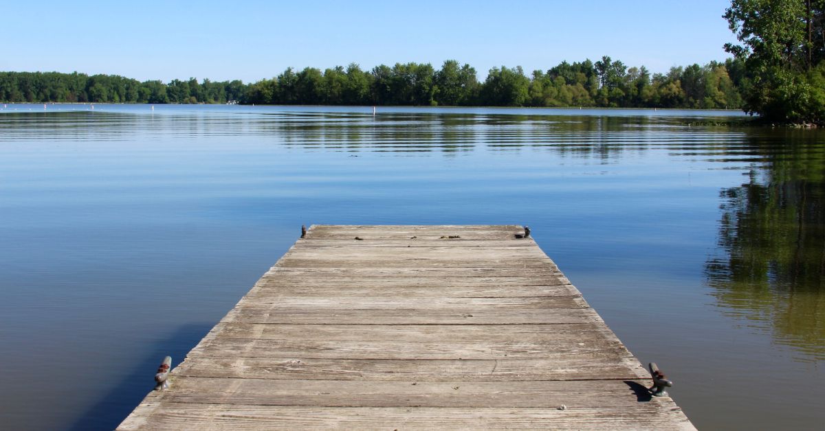 A short, wooden dock against a pristine, placid lake. The bright blue sky is reflecting in the gently rippling water.
