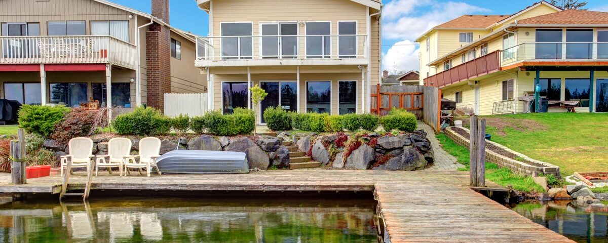 The backyard of a home with a long dock. The dock is clear along the walkway with chairs set up on one end.