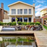 The backyard of a home with a long dock. The dock is clear along the walkway with chairs set up on one end.