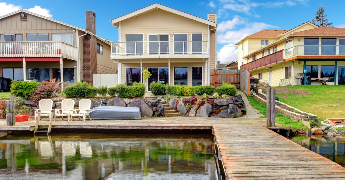 The backyard of a home with a long dock. The dock is clear along the walkway with chairs set up on one end.