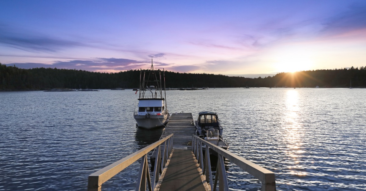 A boat dock on a peaceful lake with the sun setting in the distance. There are two boats next to the dock.