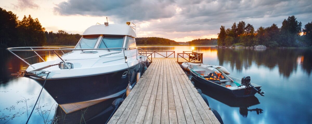 A wooden pier on a lake at sunset. There are two boats attached to the dock, one large and one small.
