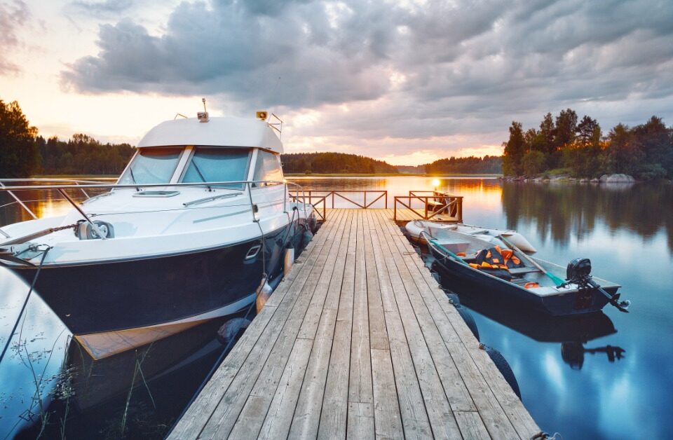A wooden pier on a lake at sunset. There are two boats attached to the dock, one large and one small.