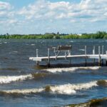 A long boat dock with benches looking out at the water. The water has a variety of waves rolling towards the dock.