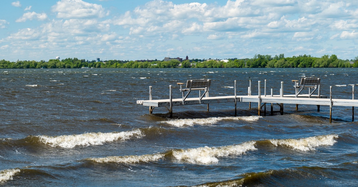 A long boat dock with benches looking out at the water. The water has a variety of waves rolling towards the dock.