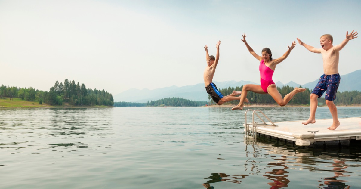 A group of children jumping off a dock into a lake. There are no other people or boats in the water around them.