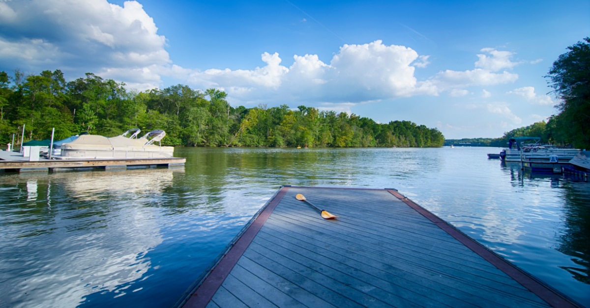 Boats attached to a dock on a lake. One of the docks has no boats near it and has a kayak paddle left on it.