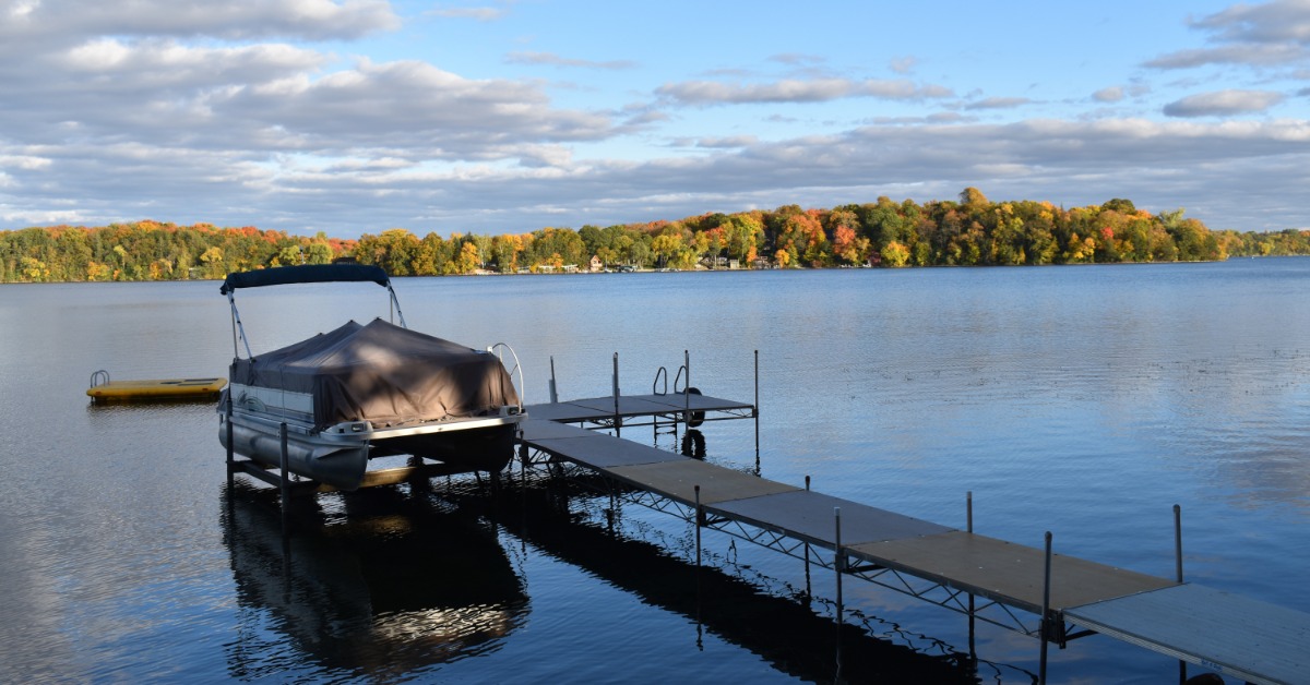 A peaceful lake with a small dock over the water. There is a covered boat on an elevated platform of the dock.