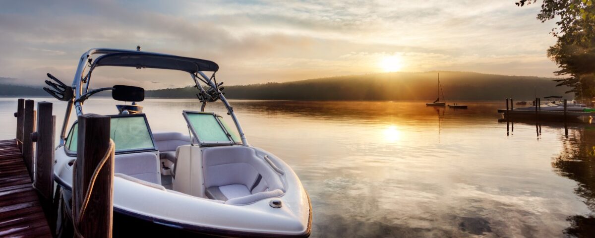 The sunrise is reflecting off a lake and the morning mist. There is a dock with a small boat tied to it.