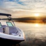 The sunrise is reflecting off a lake and the morning mist. There is a dock with a small boat tied to it.