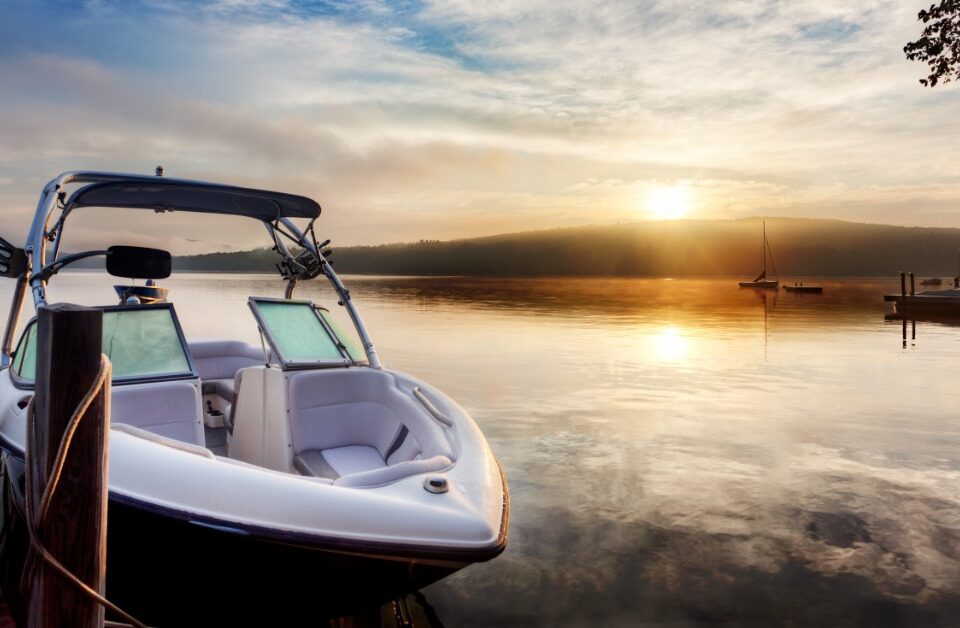 The sunrise is reflecting off a lake and the morning mist. There is a dock with a small boat tied to it.