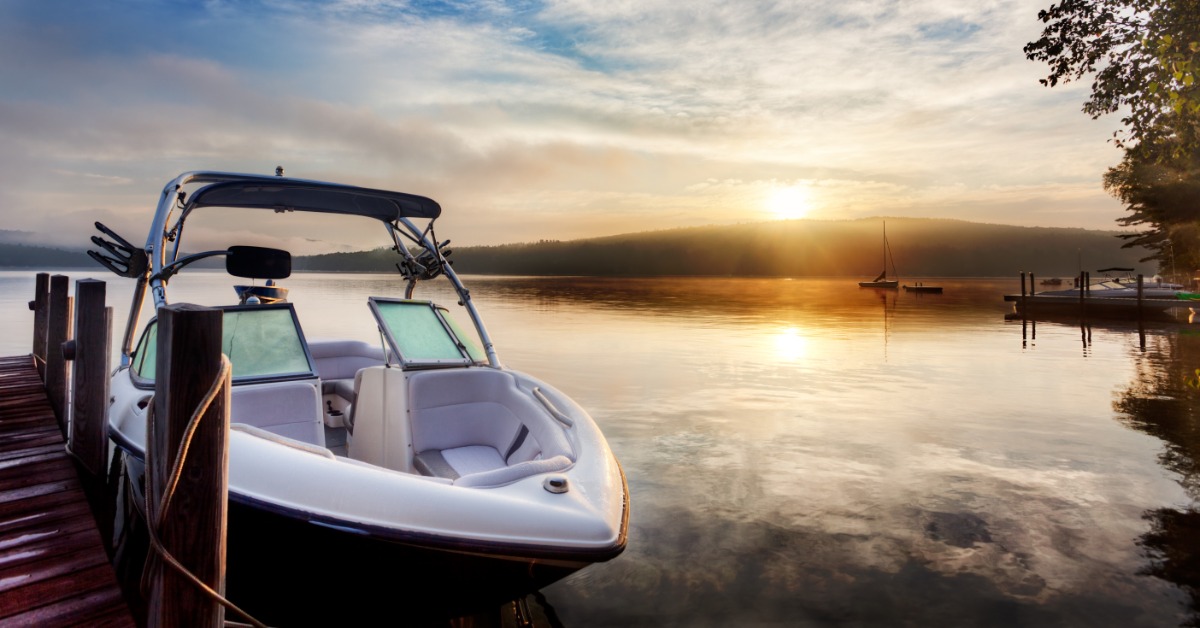 The sunrise is reflecting off a lake and the morning mist. There is a dock with a small boat tied to it.