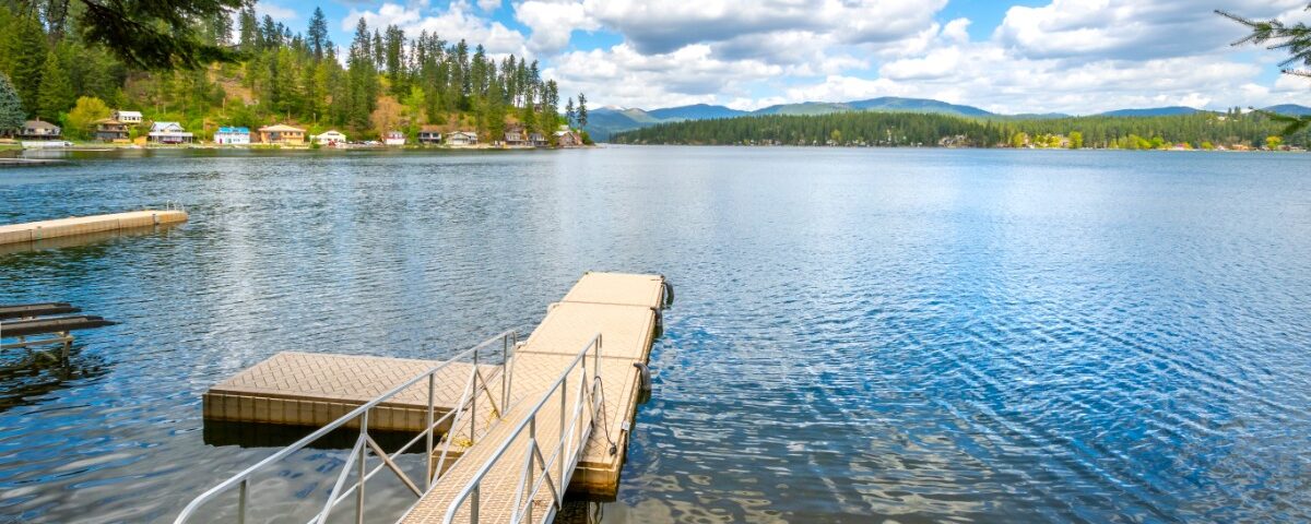 A clear lake with a small dock leading from the land to the water. A railing is attached to the ramp.