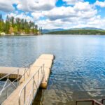 A clear lake with a small dock leading from the land to the water. A railing is attached to the ramp.
