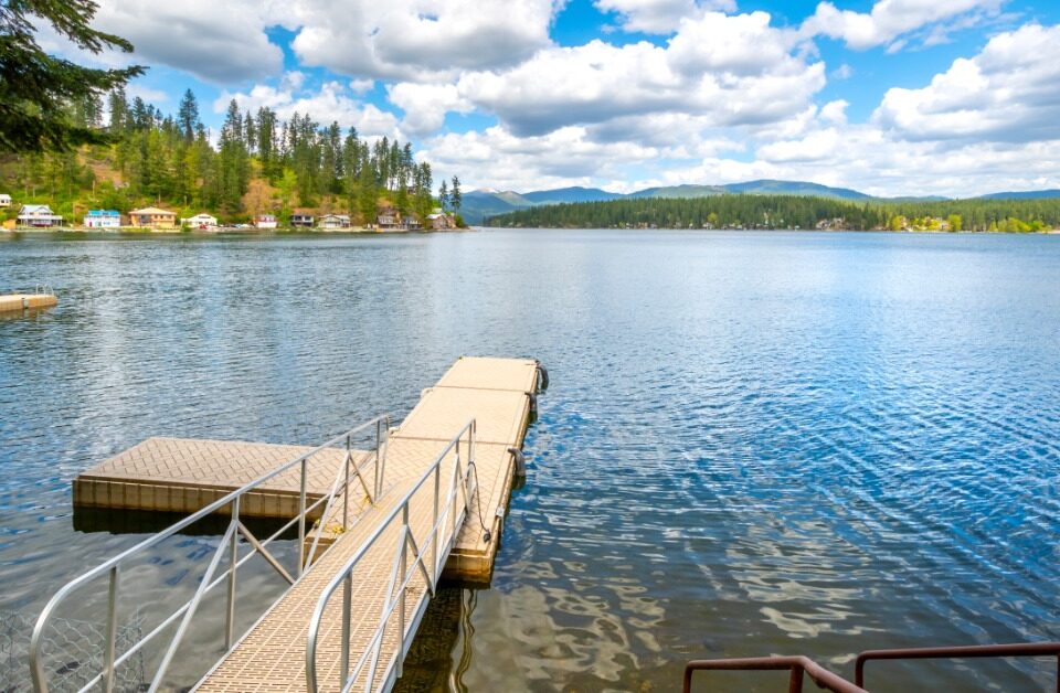 A clear lake with a small dock leading from the land to the water. A railing is attached to the ramp.